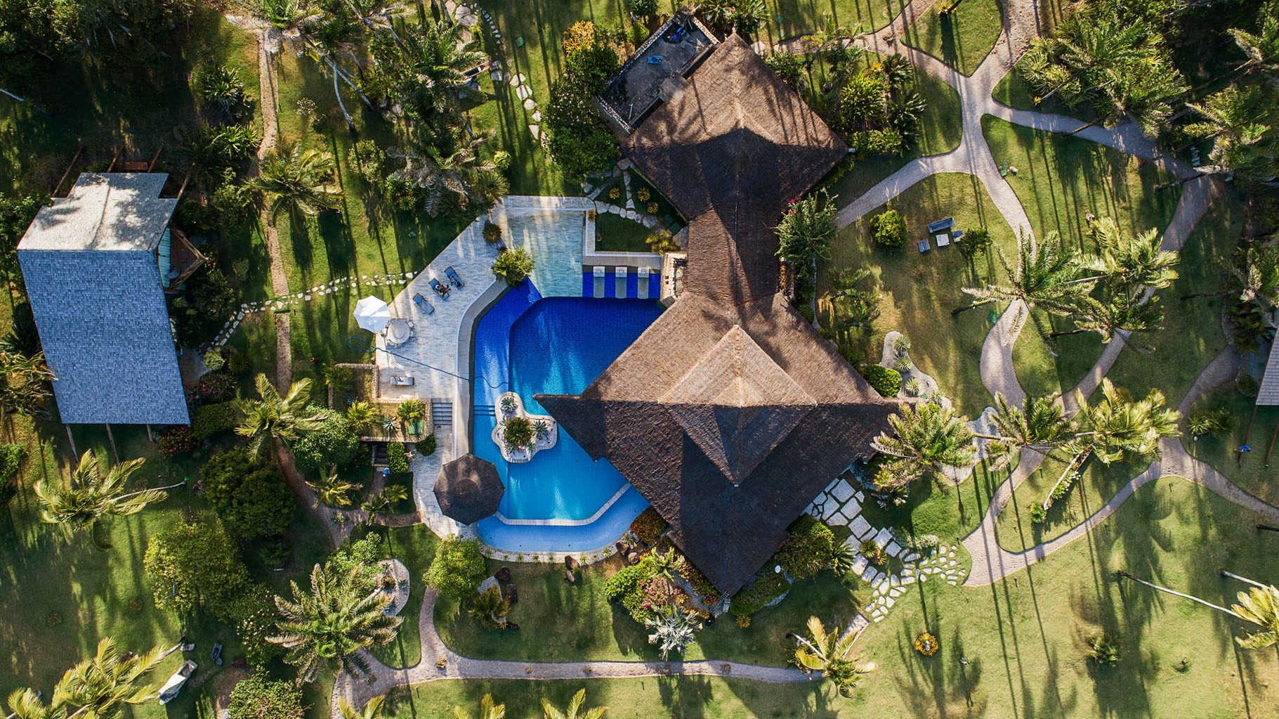 Vista aérea da Villa Taipú, mostrando piscina, telhados de palha e jardim tropical